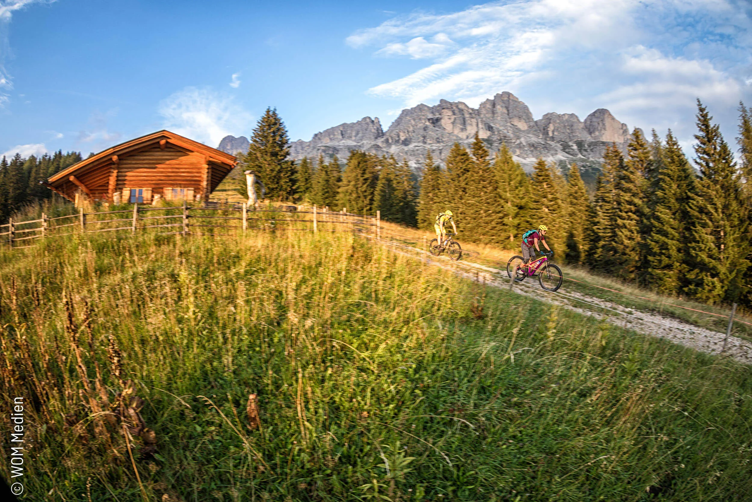 Two mountain bikers riding on a path near a mountain hut in the mountains