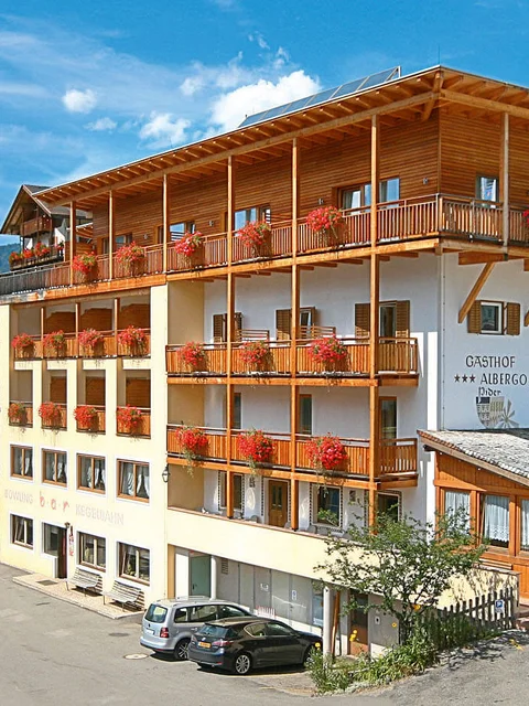 Gasthof mit roten Blumen und Bergen im Hintergrund bei klarem Himmel