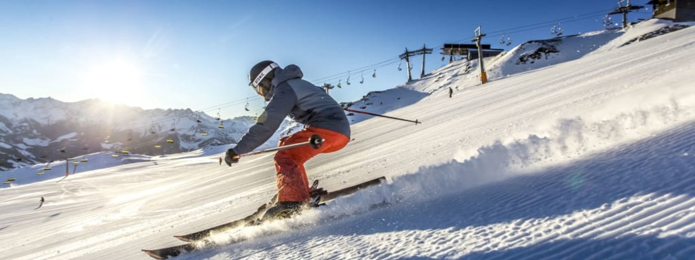 Skier skiing down a slope in a sunny snowy mountain area