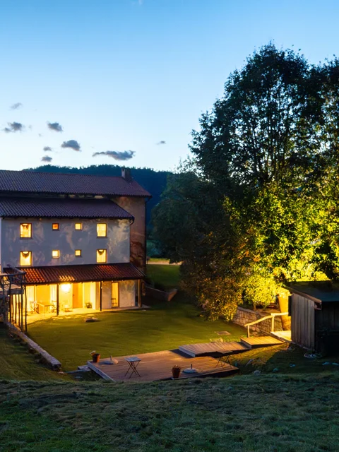Haus mit beleuchtetem Garten bei Dämmerung in einer ländlichen Umgebung