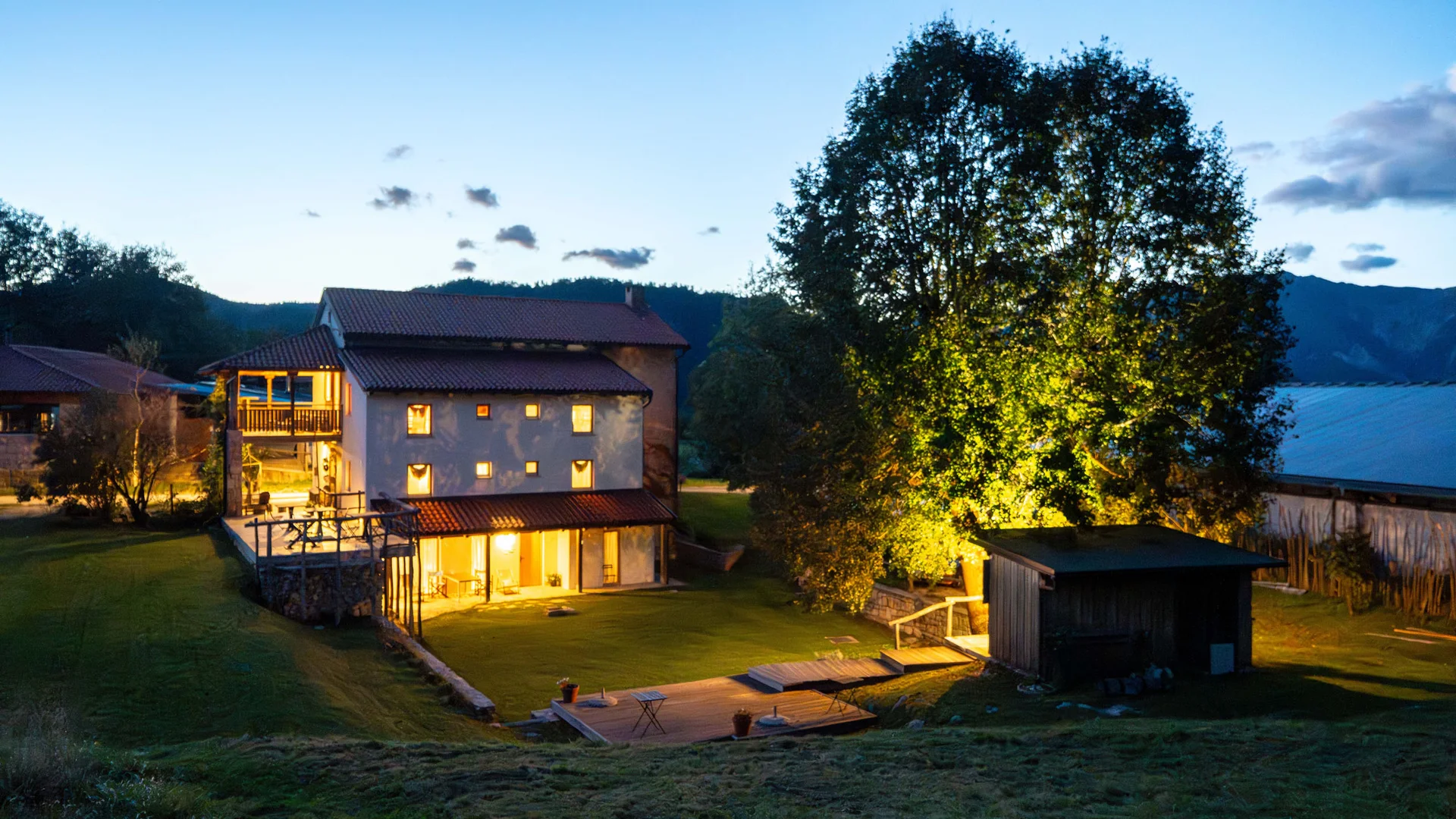 Haus mit beleuchtetem Garten bei Dämmerung in einer ländlichen Umgebung