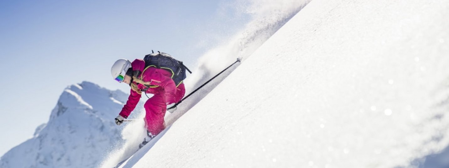 Skifahrerin in roter Kleidung fährt einen verschneiten Hang hinunter vor Bergkulisse