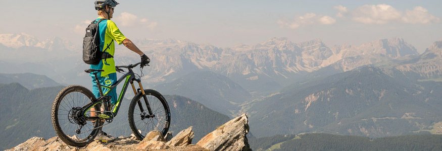 Mountainbiker mit Helm auf Felsen blickt auf Bergpanorama