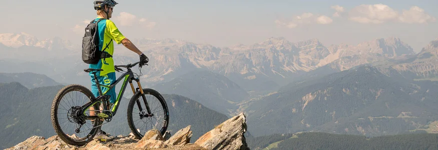 Mountainbiker mit Helm auf Felsen blickt auf Bergpanorama