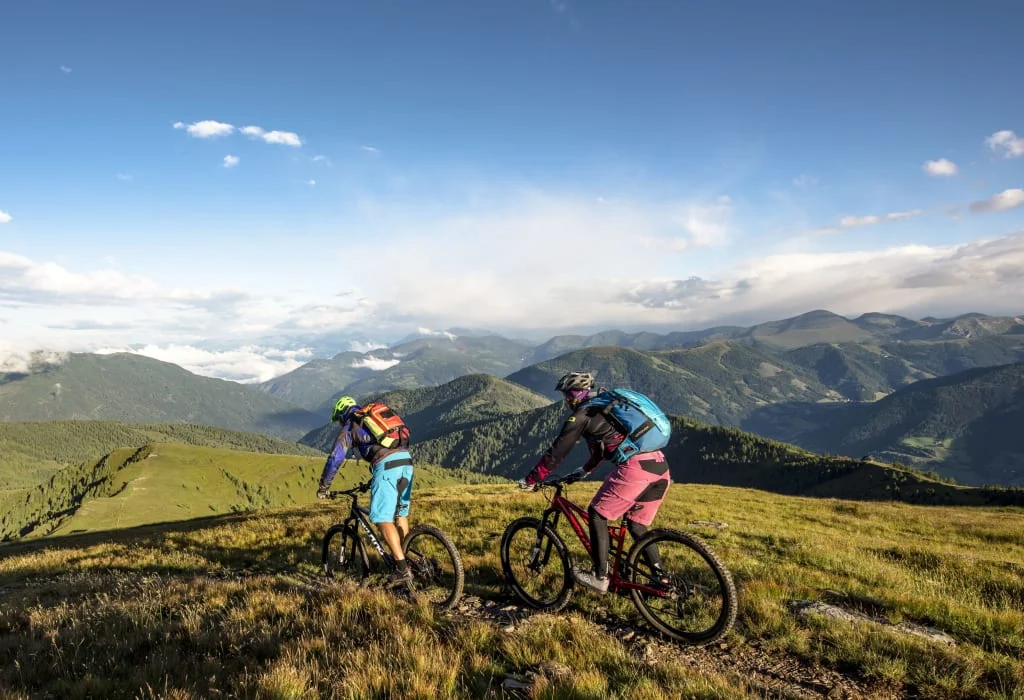 Zwei Mountainbiker auf Bergpfad mit Alpenlandschaft im Hintergrund
