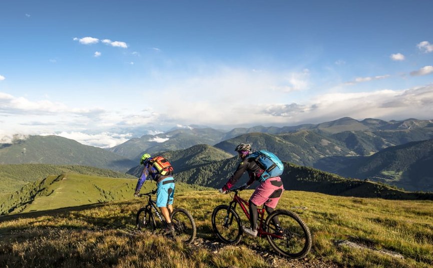 Bike & Hike mit Markus Rosenauer Zwei Mountainbiker auf Bergpfad mit Alpenlandschaft im Hintergrund