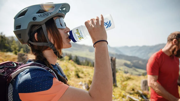 Frau mit Fahrradhelm trinkt Wasser in den Bergen