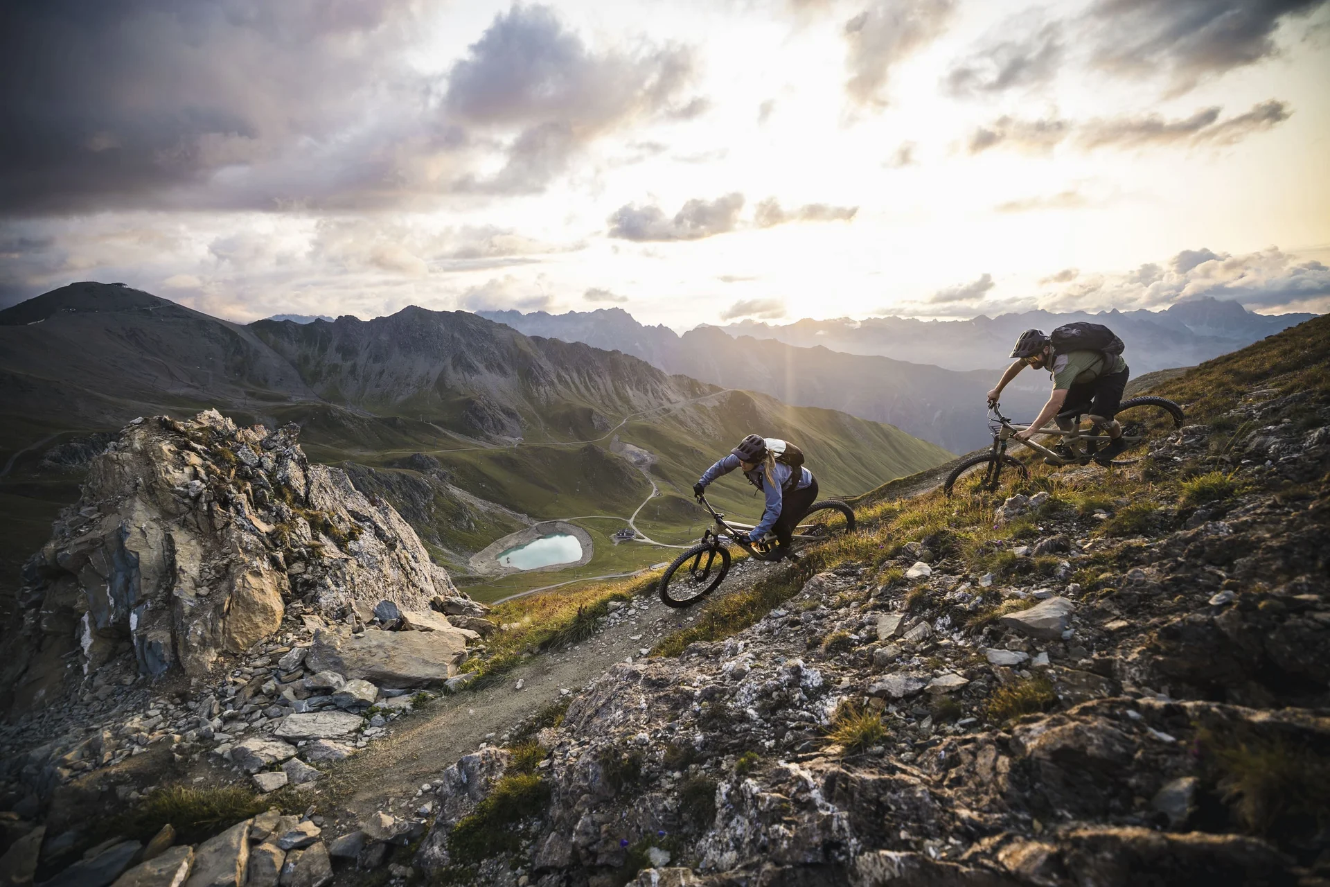 Zwei Mountainbiker fahren auf einem steilen Bergpfad mit Bergpanorama