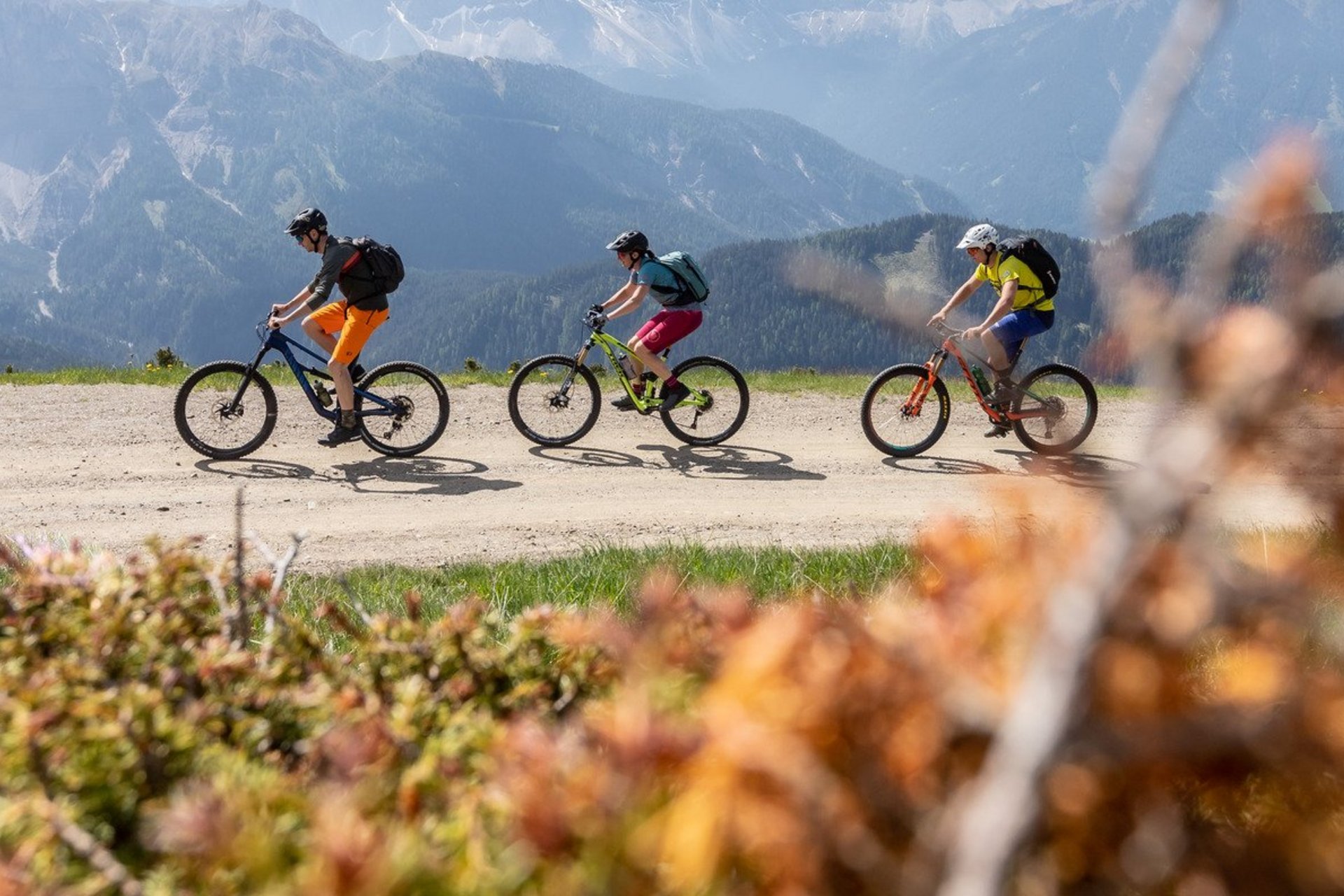 Drei Mountainbiker fahren auf einem Bergweg mit Alpen im Hintergrund