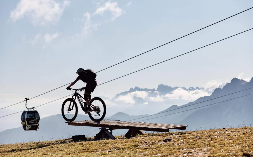 Mountainbiker bei Sprung auf Holzbühne in den Bergen bei Seilbahn