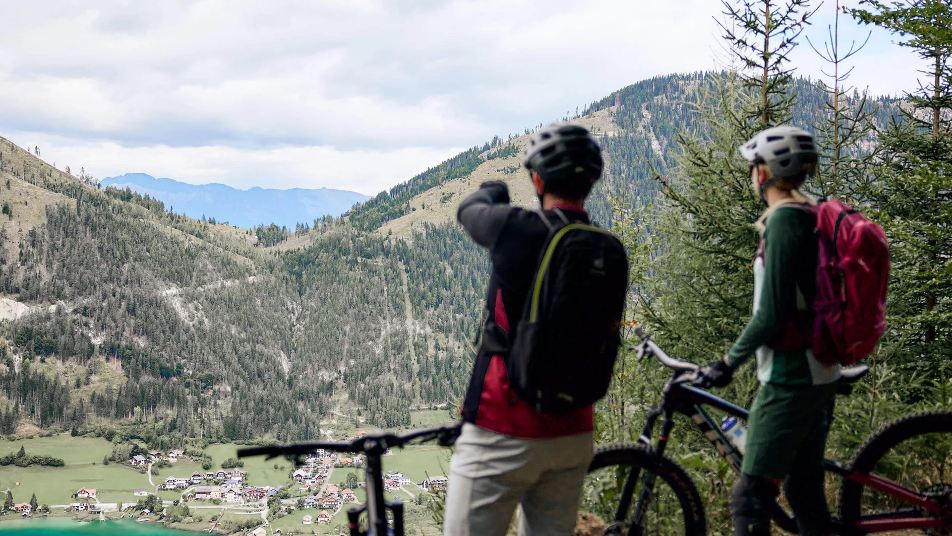 Die besten Touren & Trails der Alpen © Tobias Köhler Zwei Mountainbiker betrachten das Bergtal mit See und Dorf