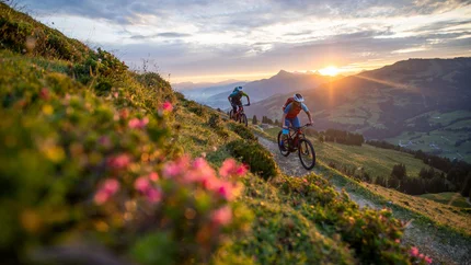 Zwei Mountainbiker fahren bei Sonnenuntergang auf einem Bergweg