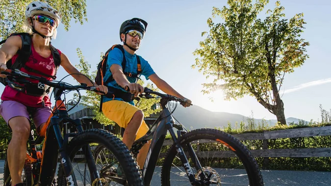 Zwei Radfahrer mit Schutzhelm fahren auf Landstraße bei sonnigem Wetter