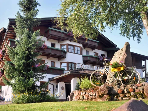 Hotel mit Balkonblumen, Fahrrad und Felsen im Garten