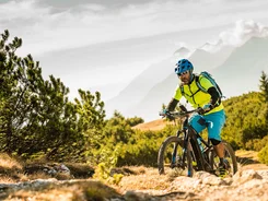 Mann fährt Mountainbike auf einem Feldweg mit Bergen im Hintergrund