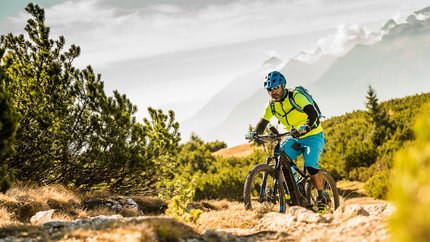 Tramin © TV Tramin - Antie Braito Mann fährt Mountainbike auf einem Feldweg mit Bergen im Hintergrund