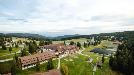 Luftaufnahme eines Ferienresorts in einer grünen, hügeligen Landschaft mit Wald