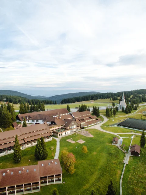 Luftaufnahme eines Ferienresorts in einer grünen, hügeligen Landschaft mit Wald