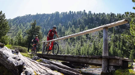 Ein Herbst-Wochenende in San Vigilio © Norman Bielig Zwei Mountainbiker fahren bei sonnigem Wetter über eine Holzbrücke im Wald