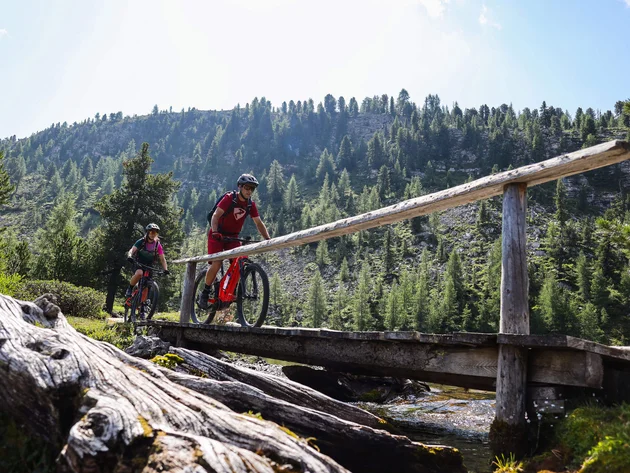 Ein Herbst-Wochenende in San Vigilio © Norman Bielig Zwei Mountainbiker fahren bei sonnigem Wetter über eine Holzbrücke im Wald