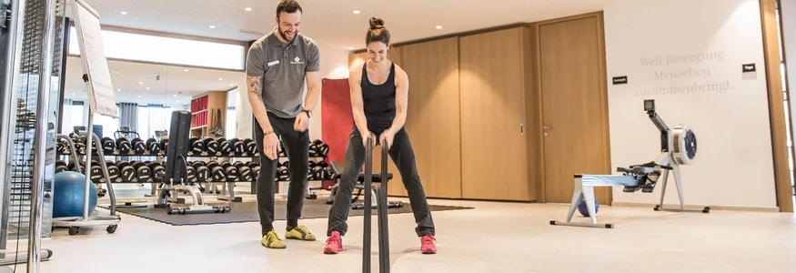 Frau trainiert mit Schlachtseilen im Fitnessstudio mit Trainer