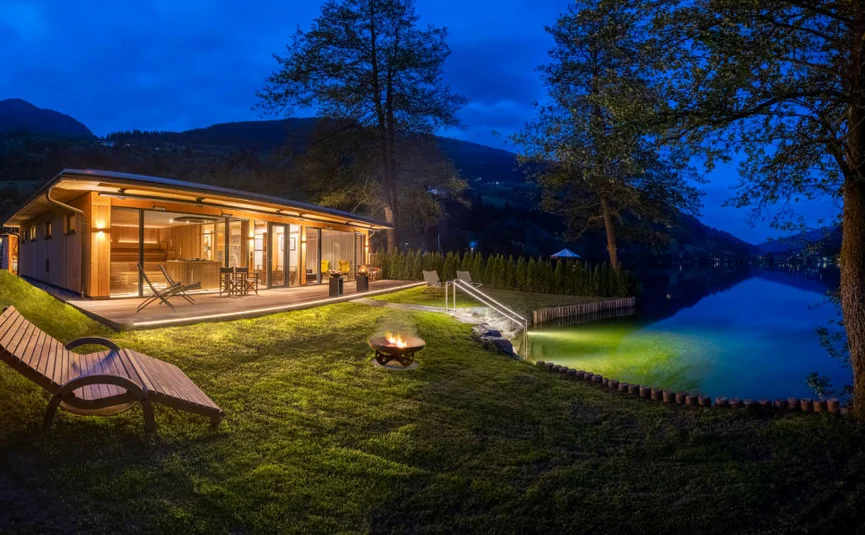Illuminated lake house with garden and fire pit at night