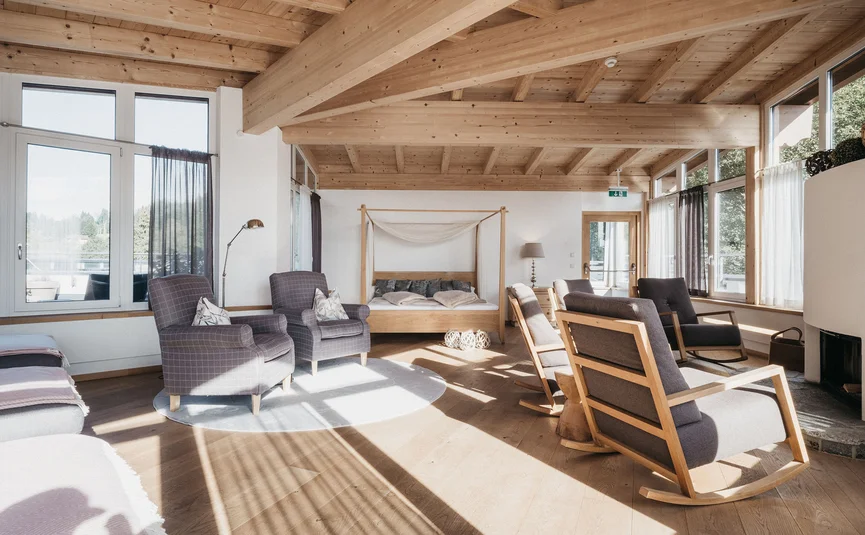 Helles Wohnzimmer mit Holzbalkendecke, Sesseln, Schaukelstühlen und einem Doppelbett