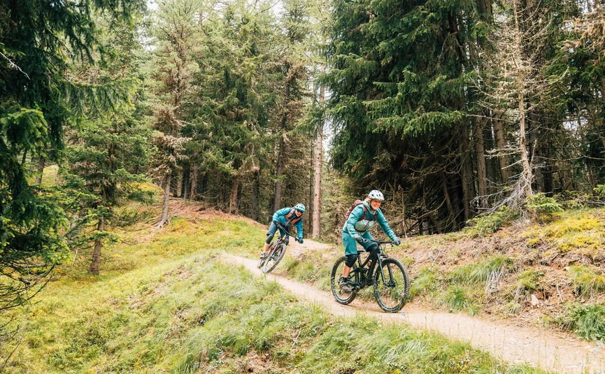 Twee personen mountainbiken op een bospad in groen gebied