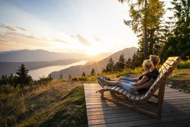 Couple sitting on wooden benches enjoying sunset over mountains and lake