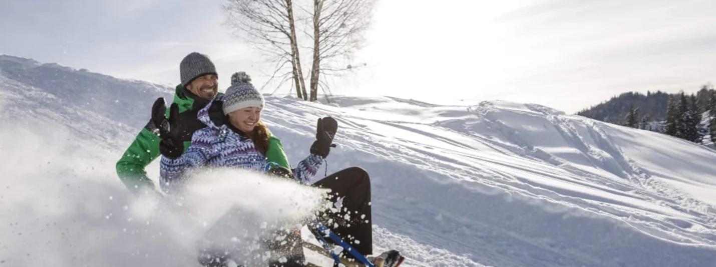 Stel lacht terwijl ze van een besneeuwde heuvel sleeën