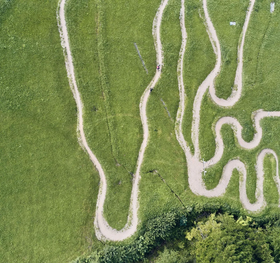 Luftaufnahme kurviger Mountainbike-Strecke im Grünen mit Fahrern