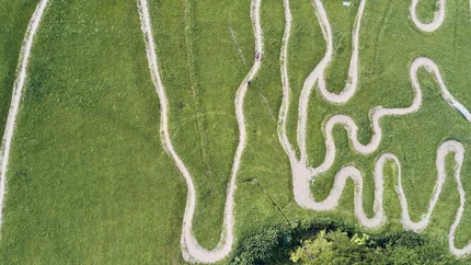 Luftaufnahme kurviger Mountainbike-Strecke im Grünen mit Fahrern