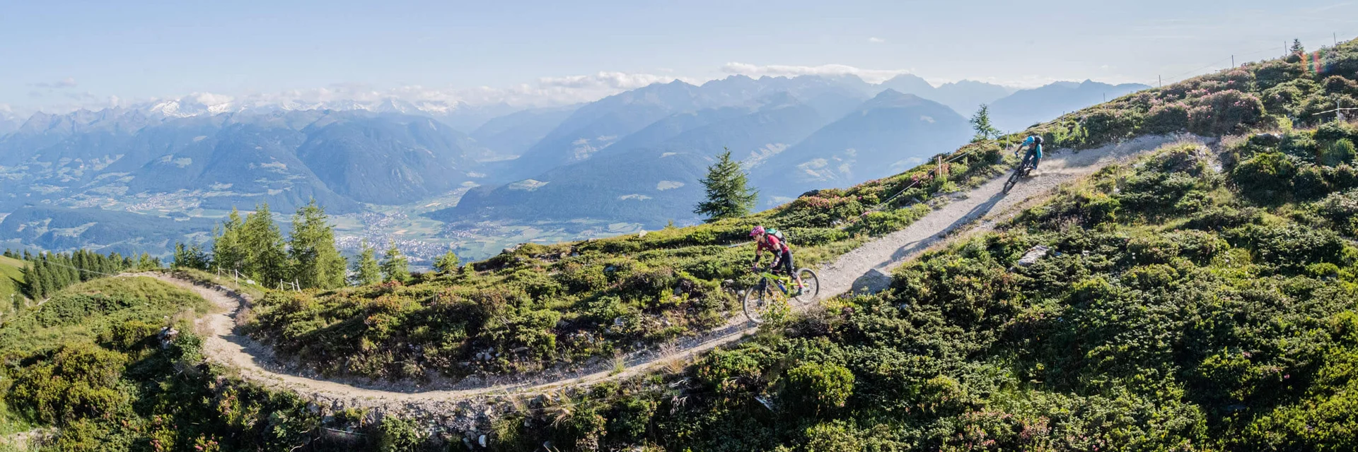 Mountain bikers riding on a mountain trail with alpine landscape under sunny sky