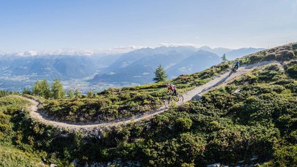 Mountainbiker fahren auf einem Bergpfad mit Alpenpanorama bei sonnigem Wetter
