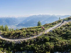 Mountainbiker fahren auf einem Bergpfad mit Alpenpanorama bei sonnigem Wetter