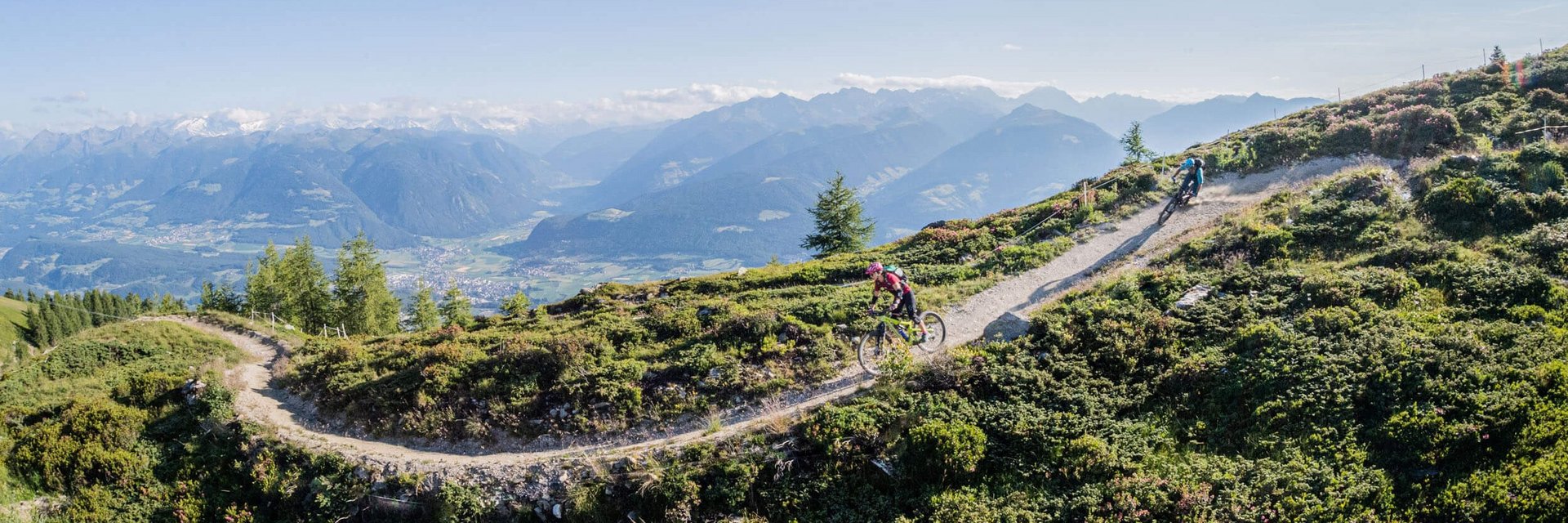 Mountain bikers riding on a mountain trail with alpine landscape under sunny sky