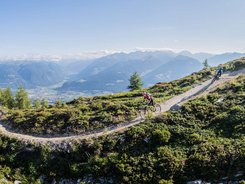 Mountain bikers riding on a mountain trail with alpine landscape under sunny sky