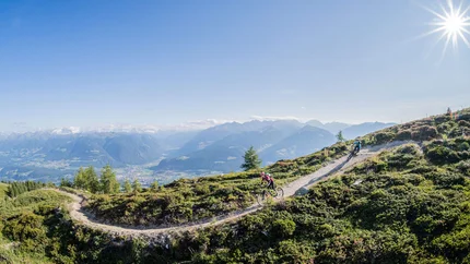 Mountainbiker fahren auf einem Bergpfad mit Alpenpanorama bei sonnigem Wetter