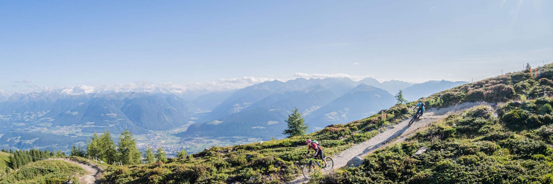 Mountain bikers riding on a mountain trail with alpine landscape under sunny sky