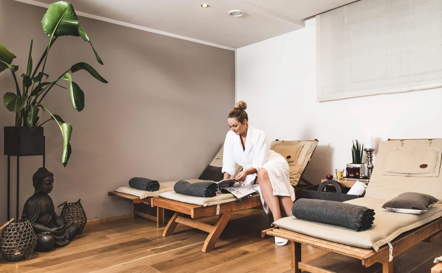 Frau im Bademantel liest entspannt Zeitschrift auf Liege im Wellnessraum
