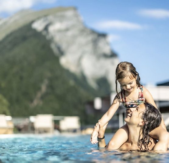 Vader speelt met dochter in buitenzwembad met berg op de achtergrond