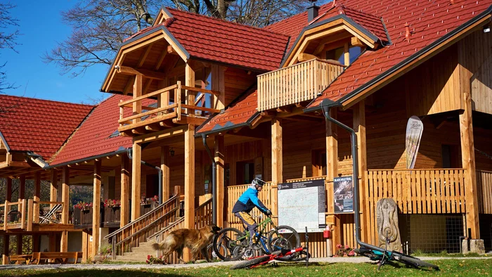 Person mit Fahrrad neben Holzhaus mit rotem Dach und Hund im Garten