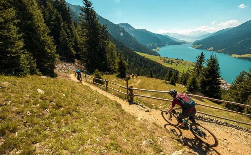 Mountainbiker fahren auf einem Pfad mit Bergsee und Bergen im Hintergrund