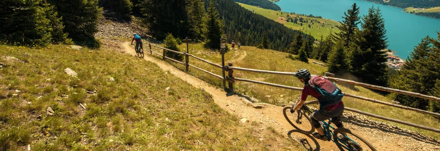 Mountainbiker fahren auf einem Pfad mit Bergsee und Bergen im Hintergrund