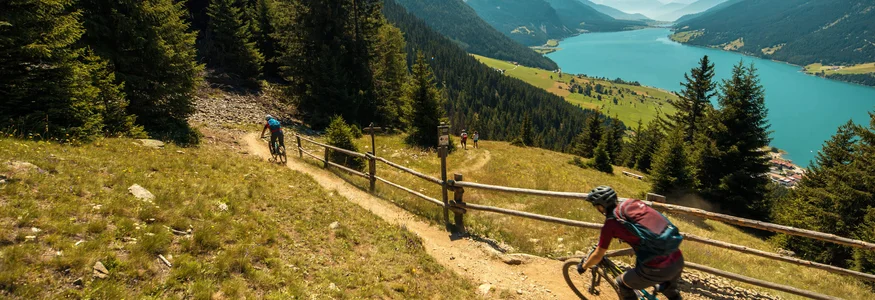 Mountainbiker fahren auf einem Pfad mit Bergsee und Bergen im Hintergrund