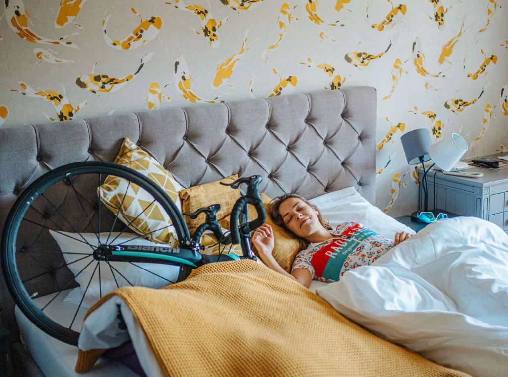 Frau schläft im Bett neben einem Fahrrad unter gelber Decke