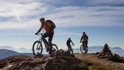 Drei Mountainbiker fahren auf einem Bergweg bei klarem Himmel