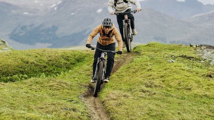 Zwei Mountainbiker fahren auf einem schmalen Pfad in bergigem Gelände