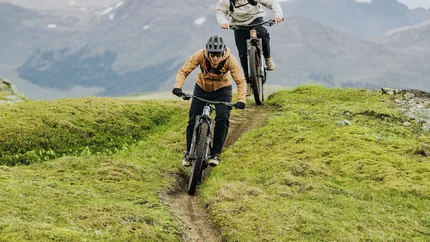Zwei Mountainbiker fahren auf einem schmalen Pfad in bergigem Gelände