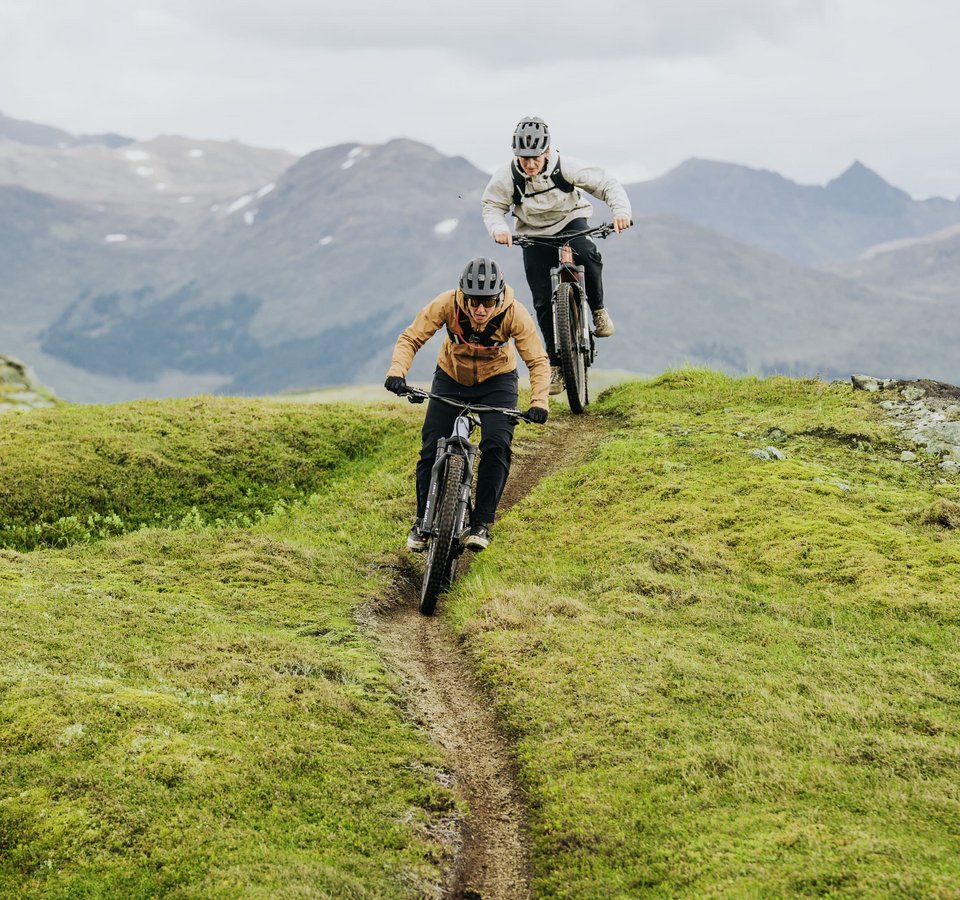 Zwei Mountainbiker fahren auf einem schmalen Pfad in bergigem Gelände